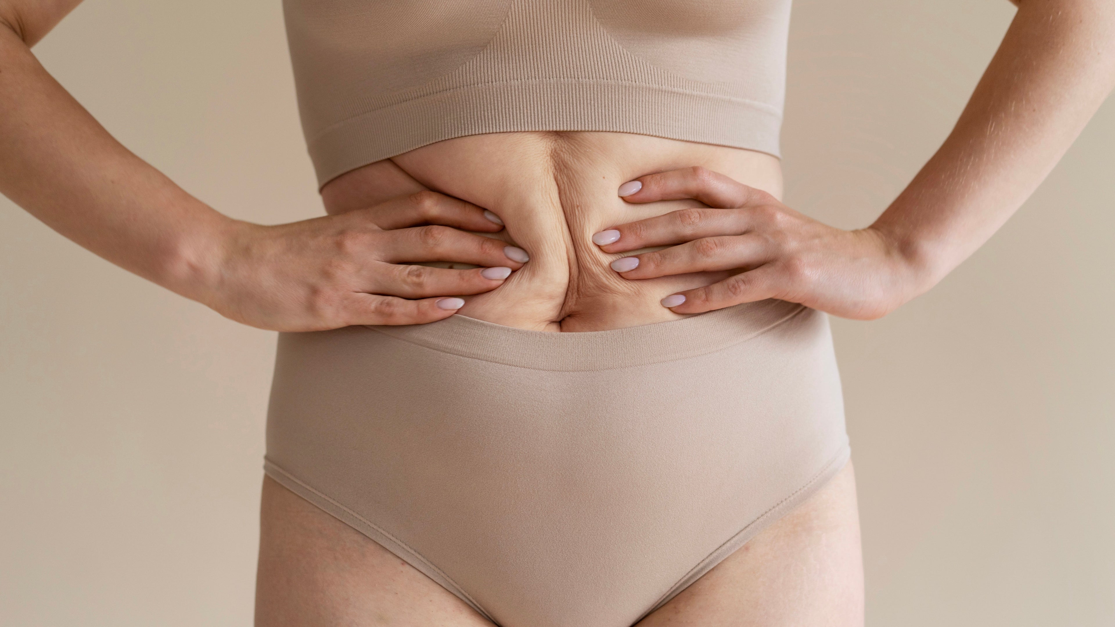 kvinde iført beige undertøj griber om sin naturlige mave
