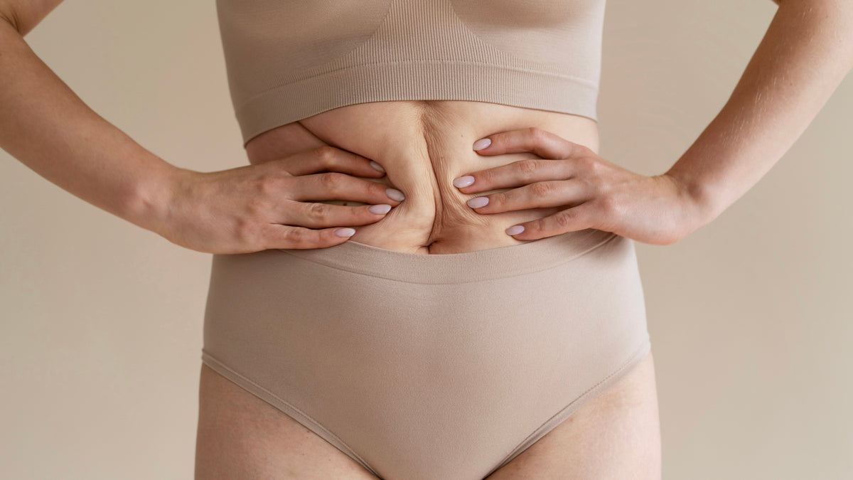 kvinde iført beige undertøj griber om sin naturlige mave